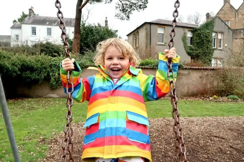 boy wearing rainbow jacket on swing