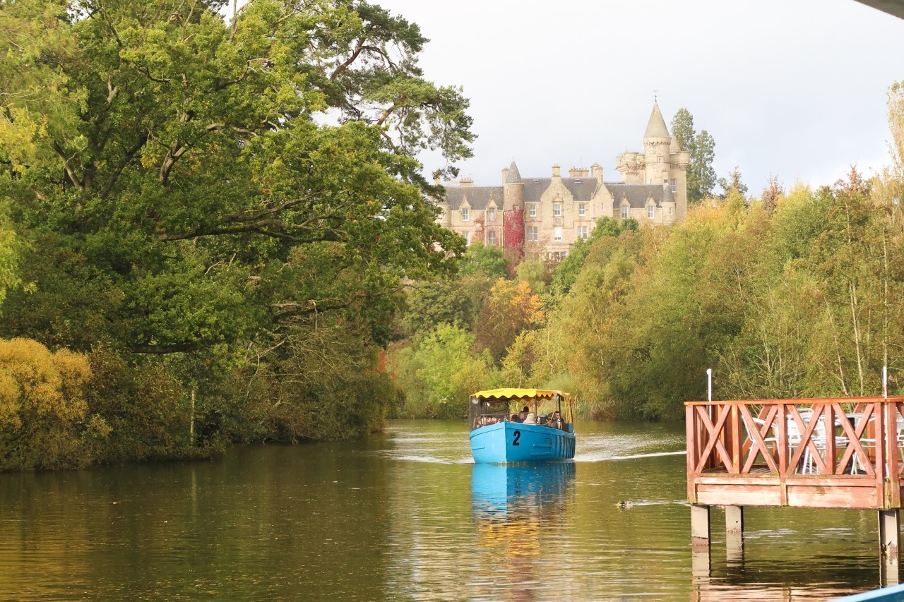 boat travelling down man made lake below a Scottish mansion house