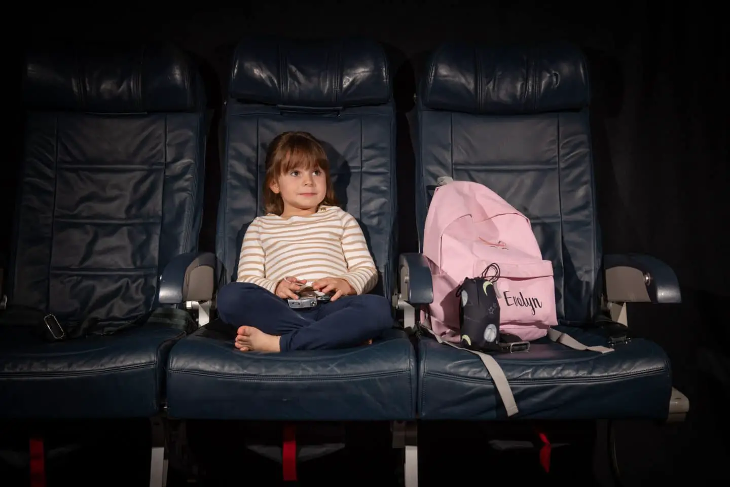 child sitting on plane seat beside bag