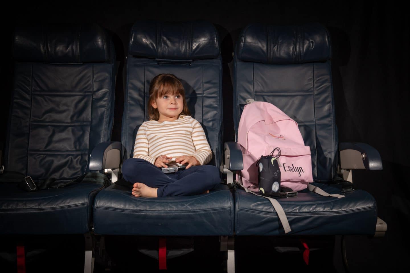 child sitting on plane seat beside bag