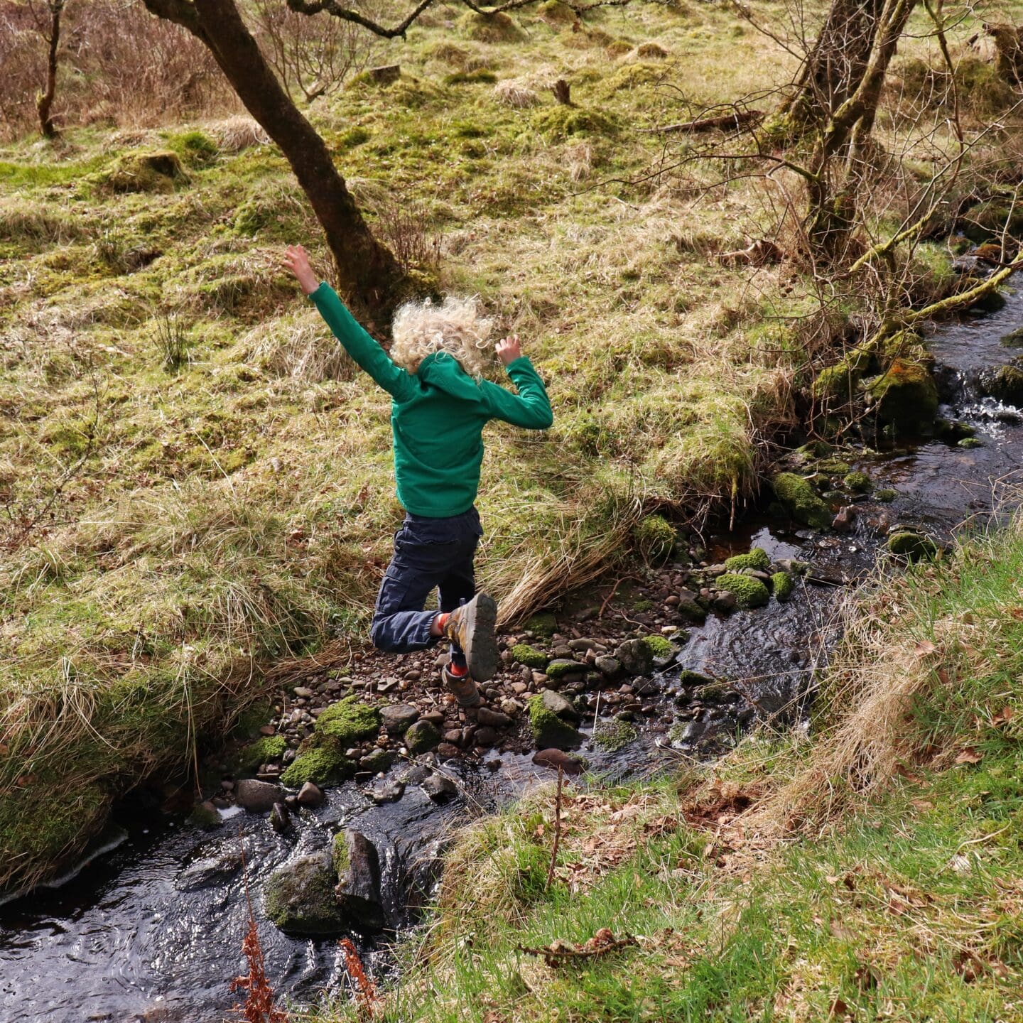 child jumping over a small burn