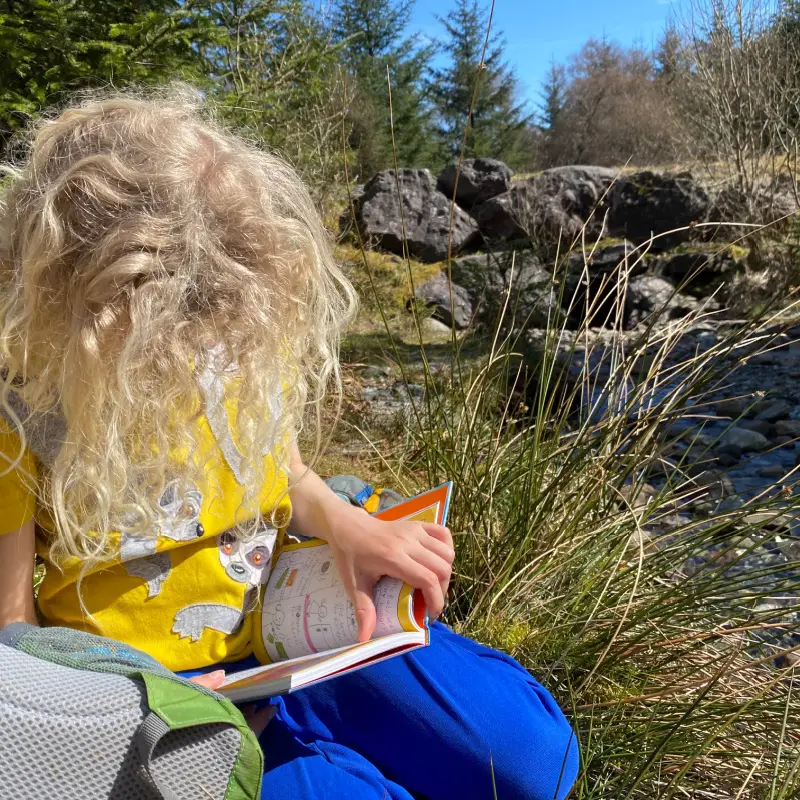 child reading a book by a stream