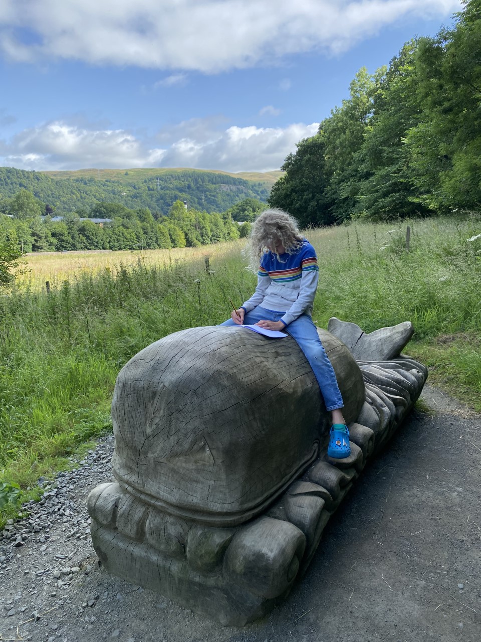 child drawing whilst sitting on a carved wooden whale