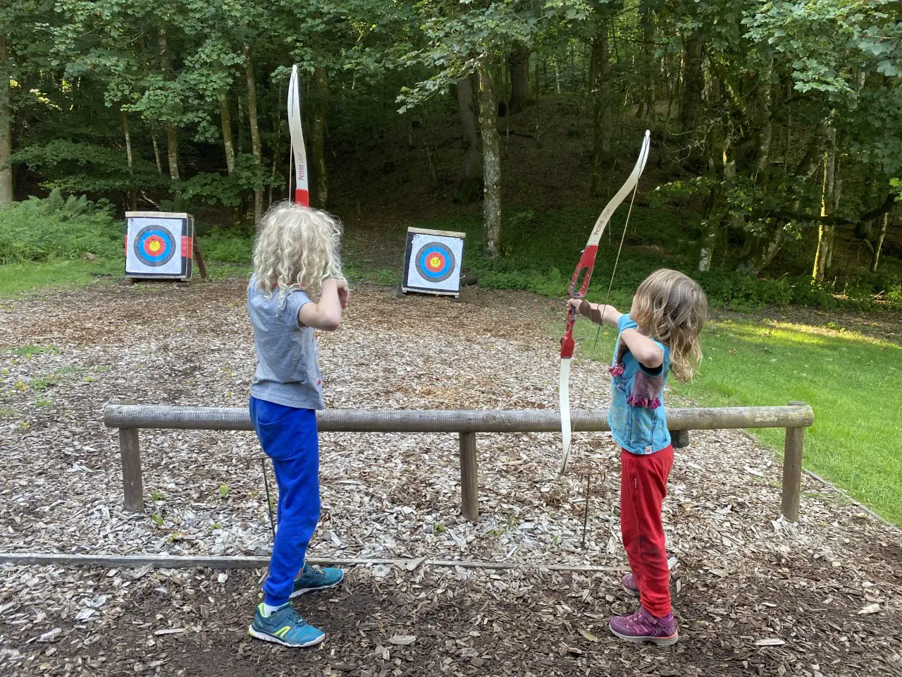2 young children holding up archery bows and shooting arrows at a boss