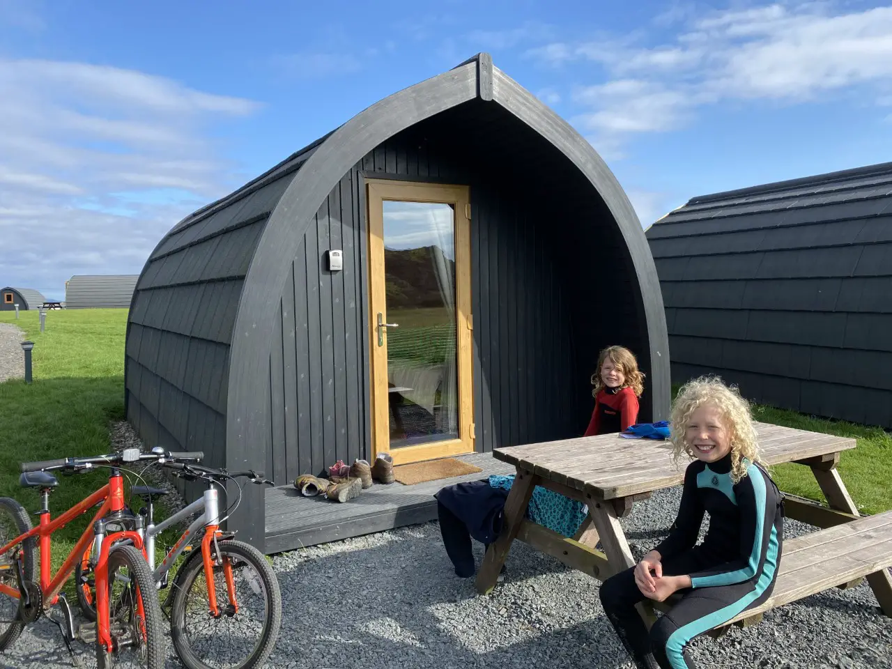 Iona pods on Isle of Iona with 2 children sitting at a picnic bench and 2 bikes beside them