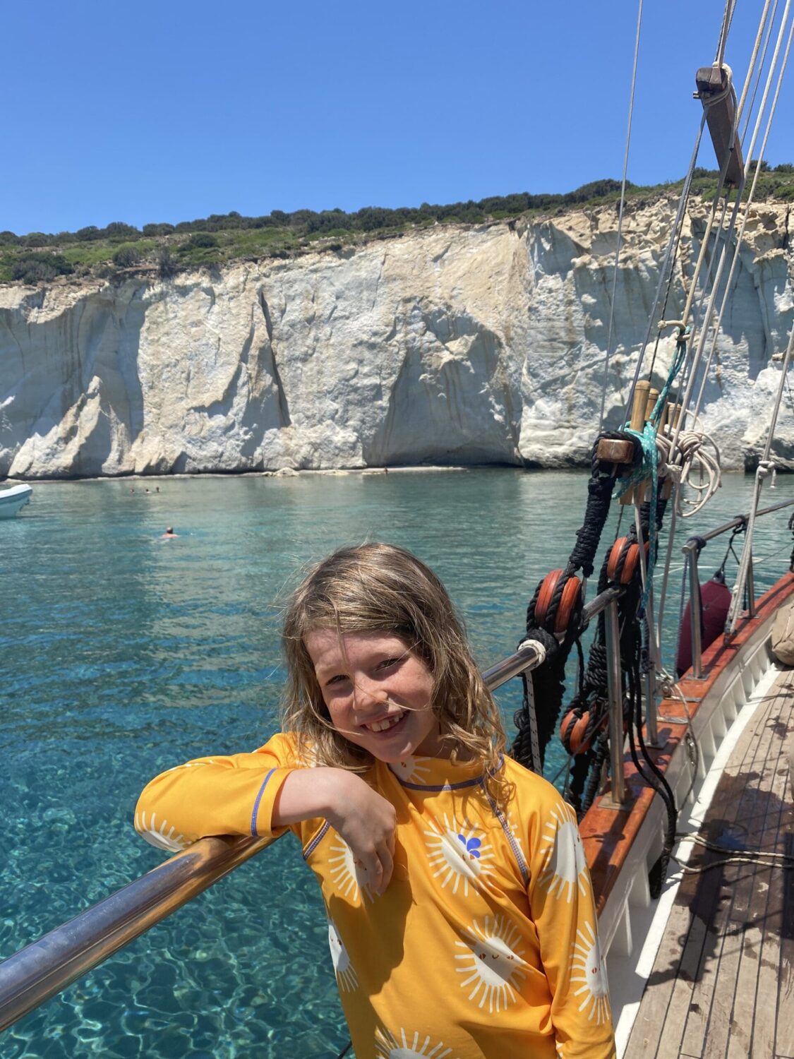 Child on a wooden snail boat with turquoise sea and white rock