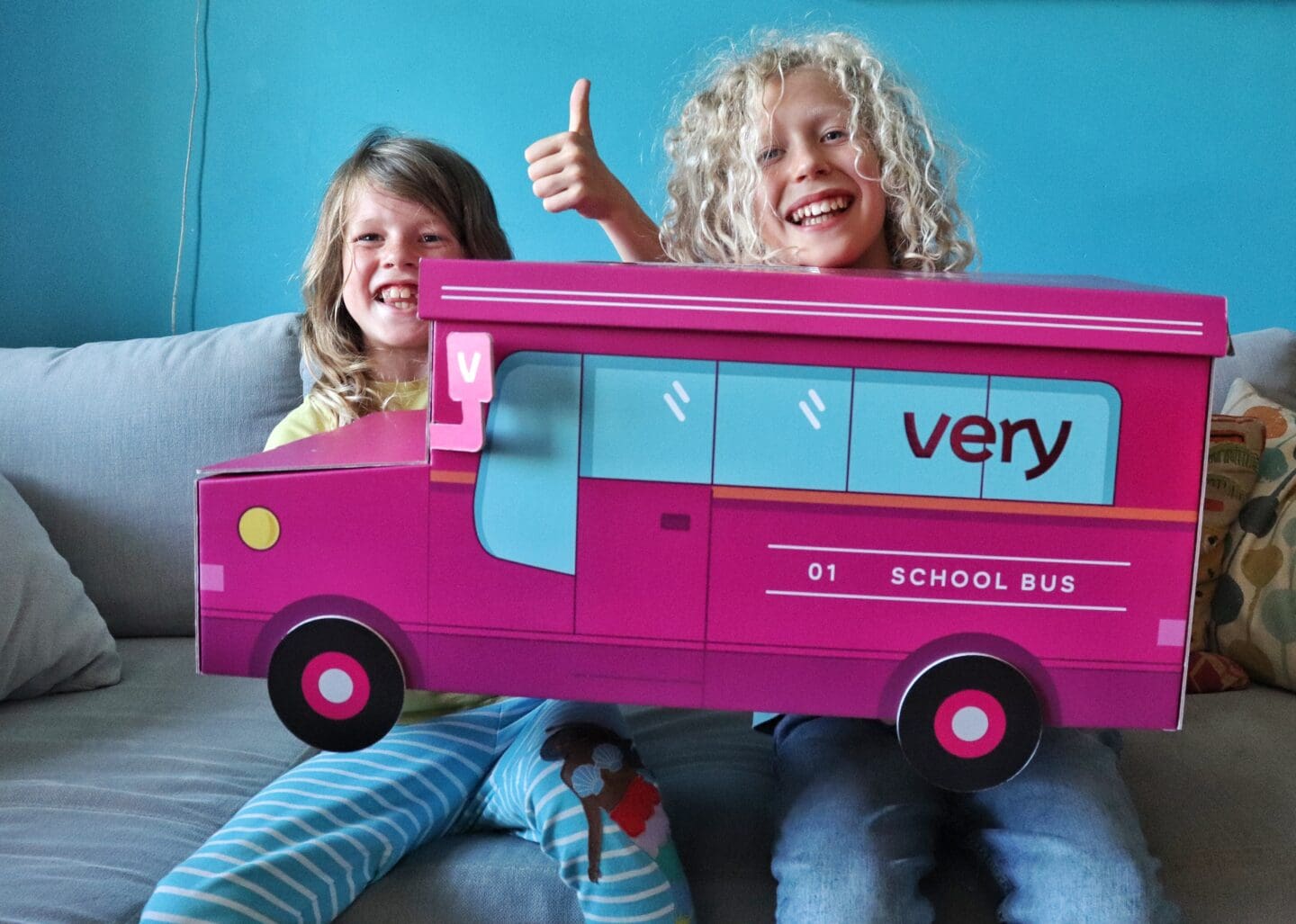 2 children holding a pink cardboard school bus with Very on the side