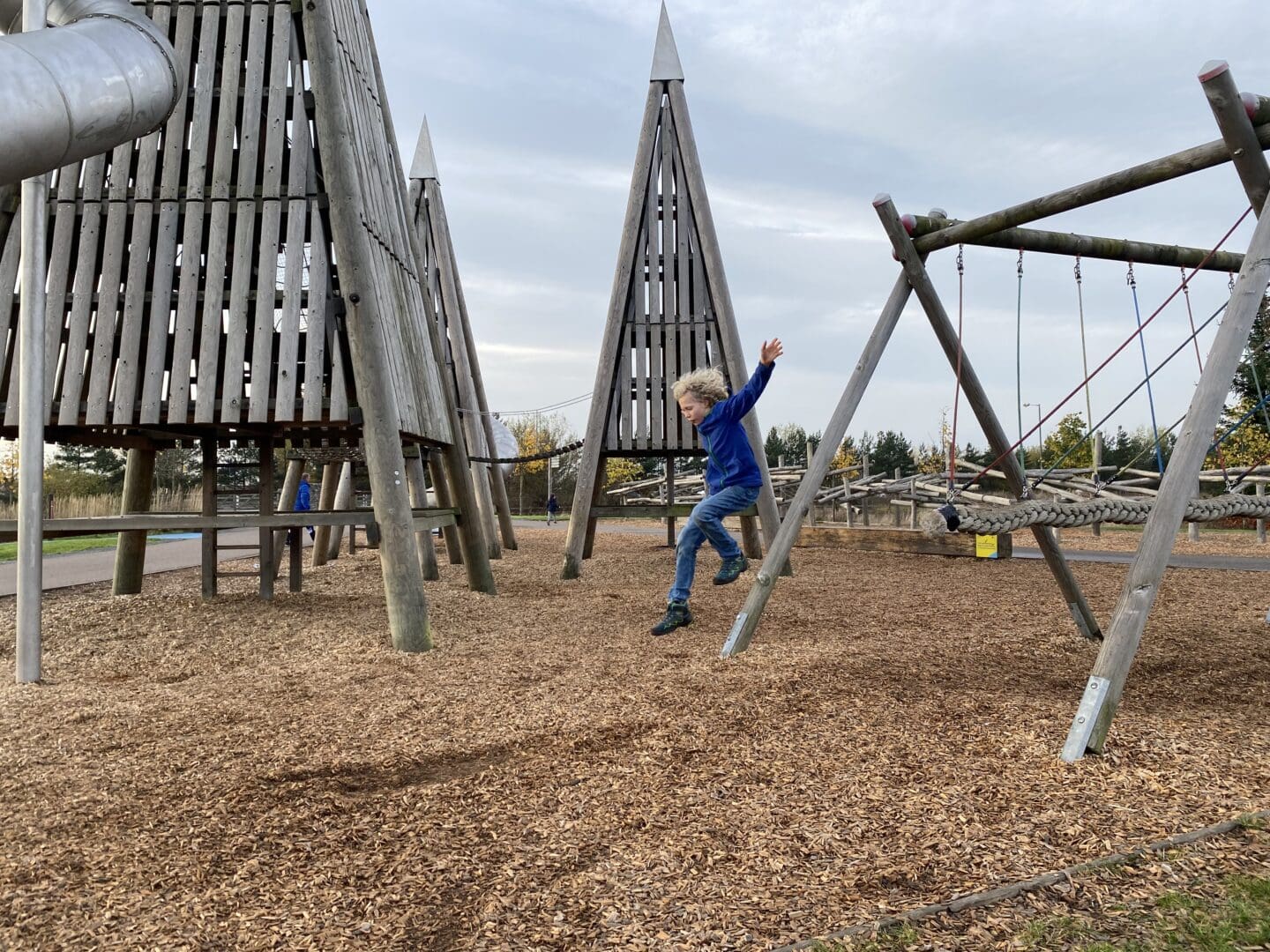 Child jumping off rope swing at play park