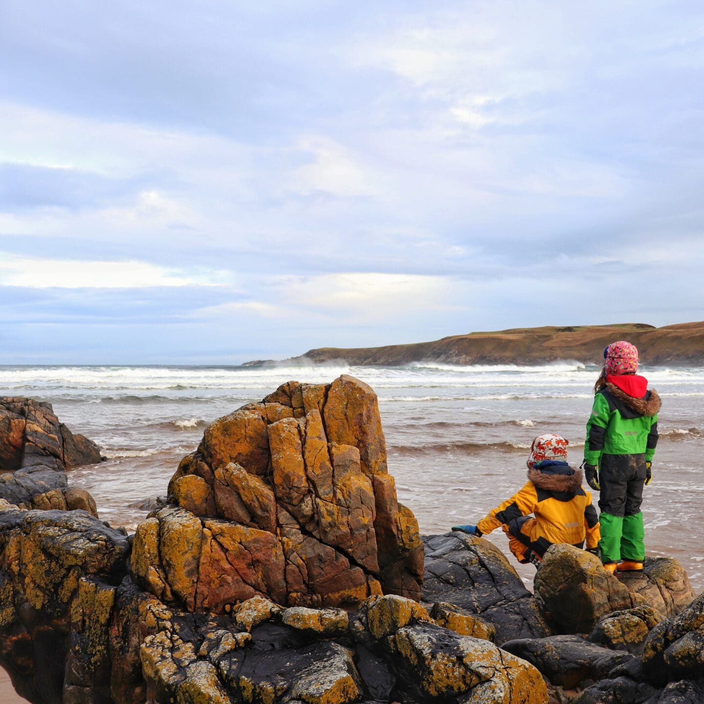 Children beside rocks looking out at waves on Scottish beach