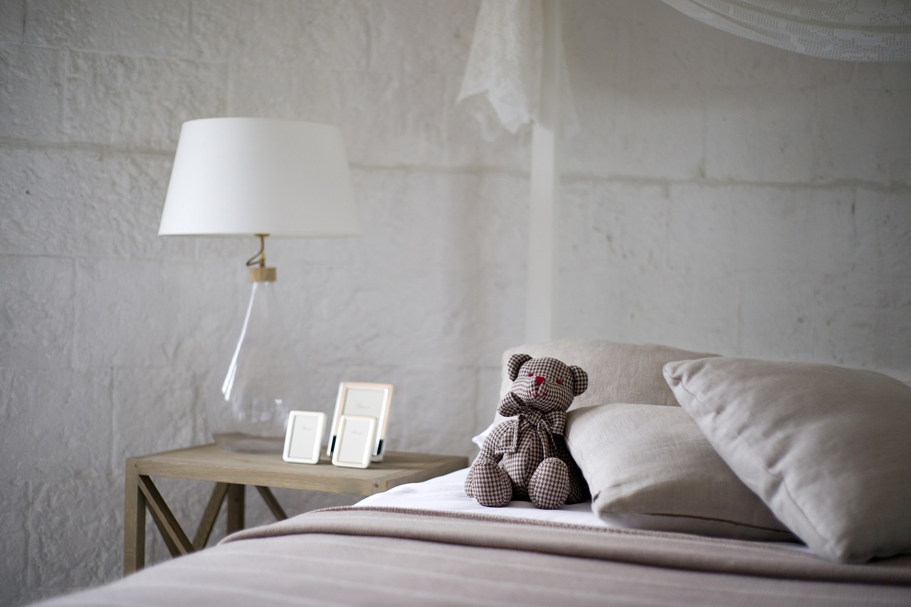 Bedroom with pillow and teddy, lamp on bedside table and brick walls