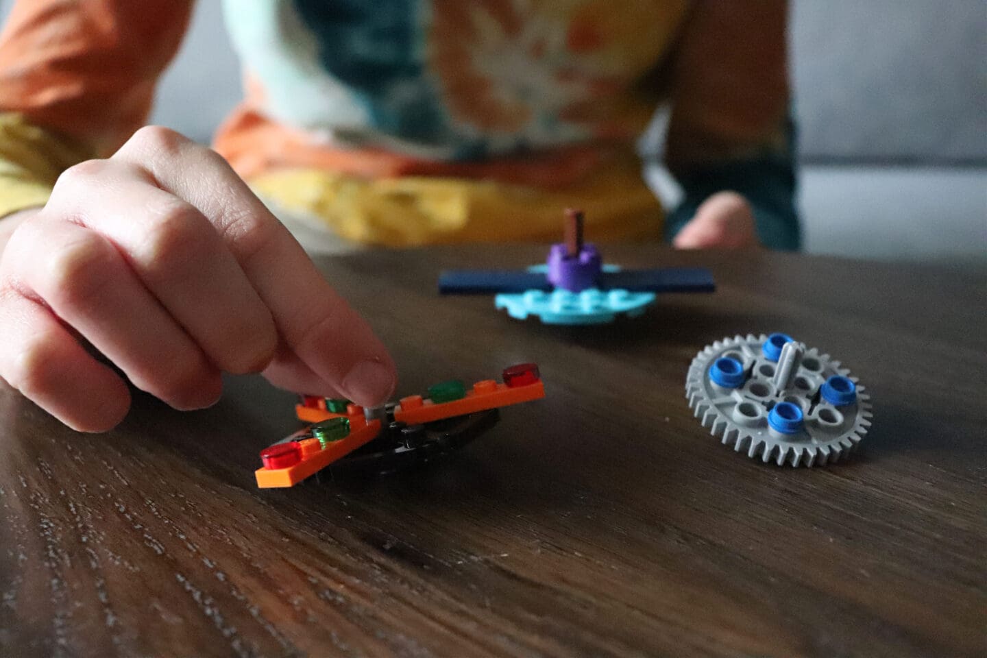 Children playing with Lego spinning tops on a brown wooden table